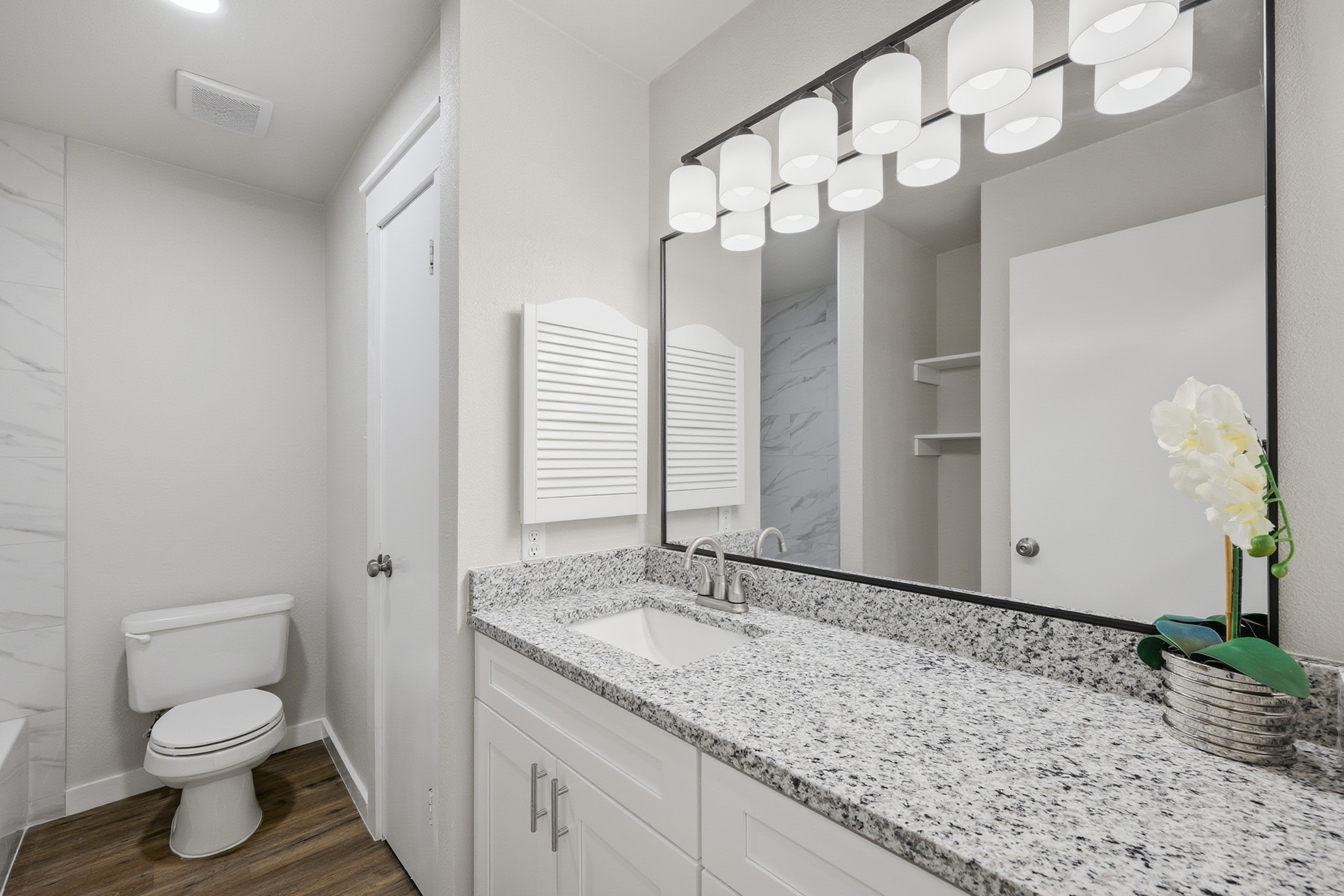 Secondary bathroom with granite countertop, undermount sink, modern lighting bar, and marble-look tile